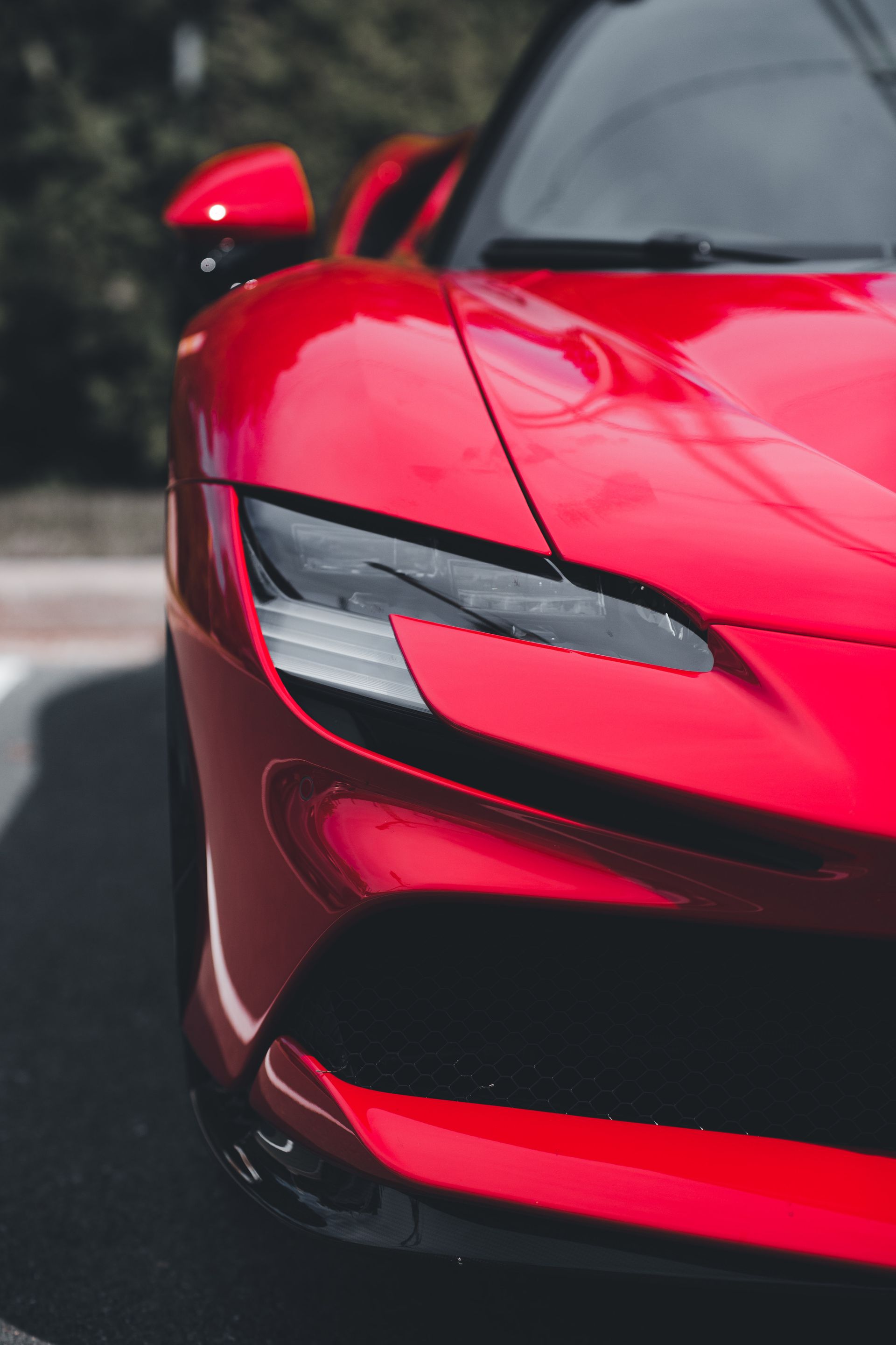 Close-up of a glossy red luxury supercar's headlight and hood, showing a deep mirror-like shine